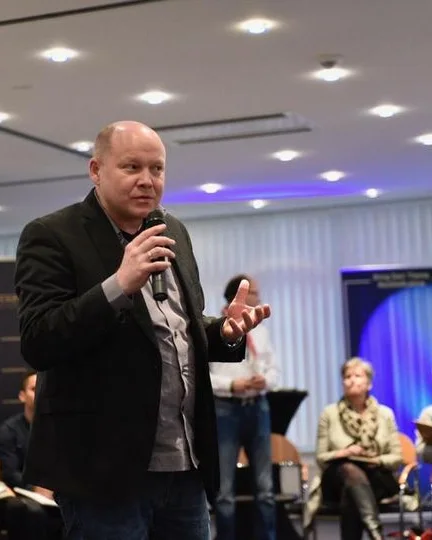 Thorsten Beckers spricht mit Mikrofon vor Publikum